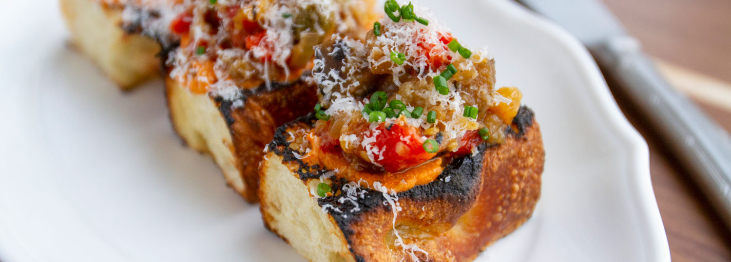 Grilled bread topped with caponata, herbs, and grated cheese